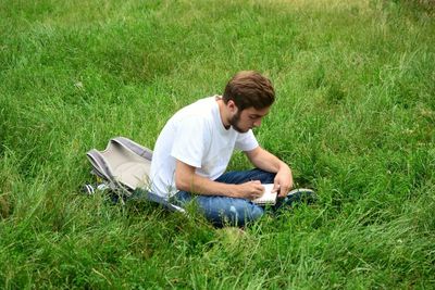 High angle view of young man making painting while sitting on grassy field