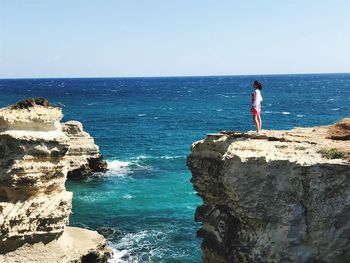 Woman standing on cliff by sea against clear sky