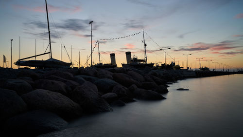 Groynes by pier in sea against sky during sunset