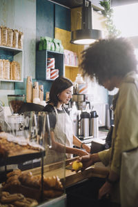 Young male customer shopping near saleswoman at checkout in convenience store