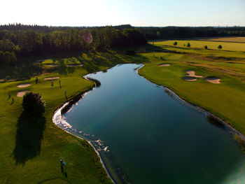 High angle view of golf course by lake against sky