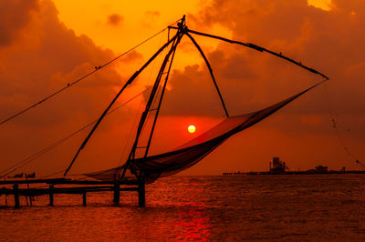 Silhouette fishing net by sea against orange sky