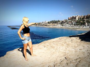 Woman pointing while standing at beach against blue sky