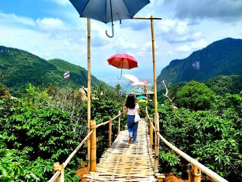 Rear view of woman walking on footbridge against sky