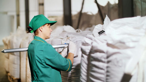 Woman, employee of agricultural enterprise, takes samples of corn grain from big bags in warehouse