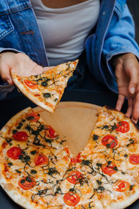 Woman taking a slice of pizza from table. big pizza without one piece. concept for italian food.