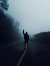 Rear view of man standing on road in foggy weather