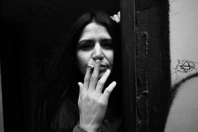 Portrait of young woman smoking cigarette while standing at doorway