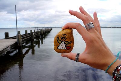 Cropped hand of woman holding stone against lake