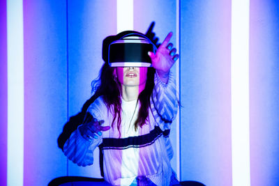 Close-up of woman wearing virtual reality standing against illuminated wall