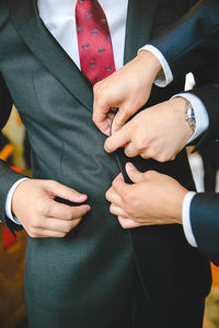 Cropped image of best man buttoning groom during wedding
