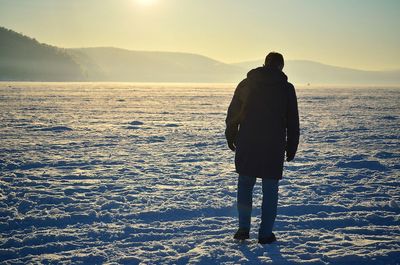 Rear view of man standing on shore against sky during sunset