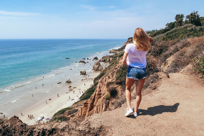 Rear view of woman sitting on cliff against sea