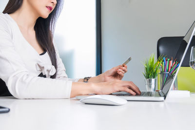 Midsection of woman using smart phone while sitting on table