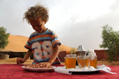 Boy standing by mint tea glass at desert against sky