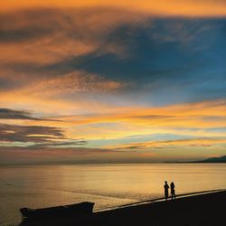 Silhouette people standing on beach against sky during sunset