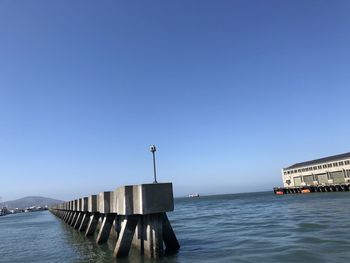 Pier over sea against clear blue sky