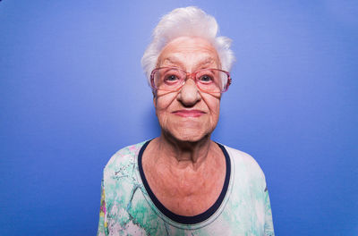 Portrait of senior woman wearing eyeglasses against blue background