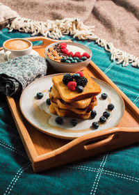 Cozy breakfast in bed, yogurt bowl with berries and nuts, french toasts, coffee cup on wooden plate