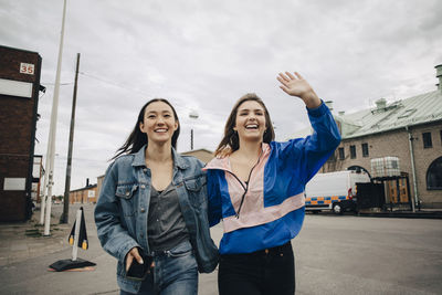 Happy young woman gesturing while walking with friend on street in city