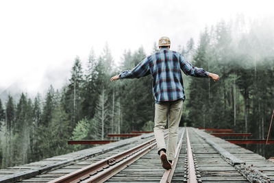 Young man balancing on railroad tracks over bridge in foggy forest