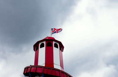 Looking up at a helter skelter with a union jack flag flying at the top against a dark cloudy sky