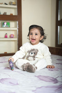 A cute little baby sitting in bed and laughing.