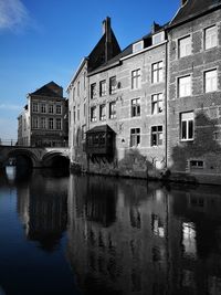 Reflection of buildings on water in canal against sky in city