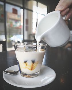 Close-up of hand pouring milk in coffee cup on table