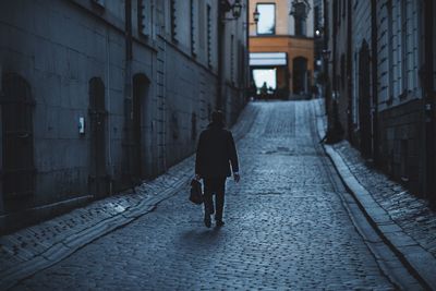 Rear view of woman walking on footpath amidst buildings