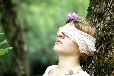 Close-up of woman with blind fold leaning on tree trunk