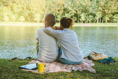 Rear view of couple relaxing at lakeshore