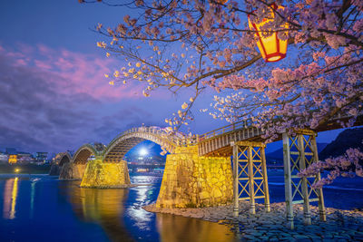 Illuminated bridge over river against sky at night