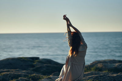 Woman standing in sea against sky during sunset