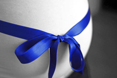 Close-up of blue ribbon tied on pregnant woman belly