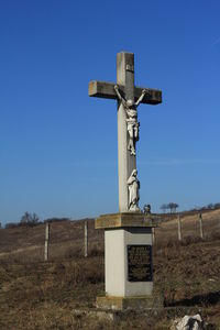 Cross in cemetery against clear blue sky