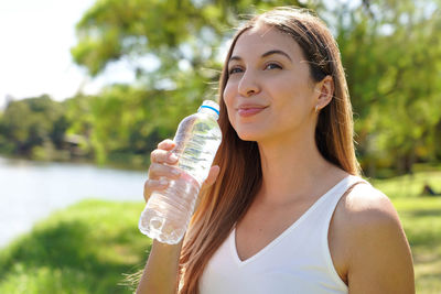 Portrait of young woman drinking water in park