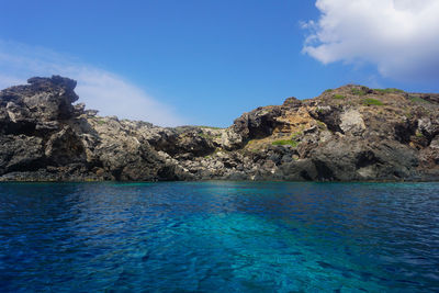 Rock formation in sea against blue sky