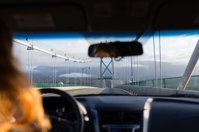 Woman driving car on suspension bridge against sky