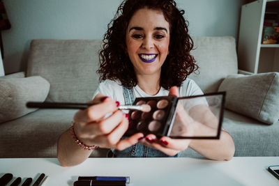 Portrait of smiling young woman using phone while sitting on sofa