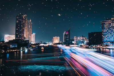 Light trails on illuminated buildings in city against sky at night