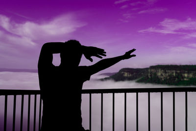 Silhouette person standing by railing against sky during sunset