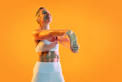 Low angle view of woman with arms raised against yellow background