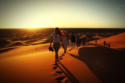 Full length of people walking on sand in desert during sunset