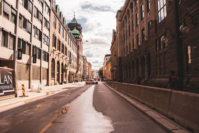 Empty road amidst buildings in city against sky