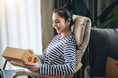 Young woman reading book while sitting on sofa at home