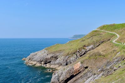 Cliff by sea against clear sky