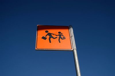 Low angle view of road sign against clear blue sky