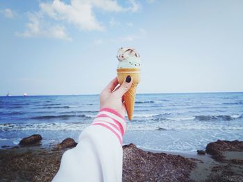 Low section of person holding ice cream at beach against sky