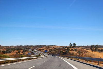 Empty road along landscape against clear blue sky